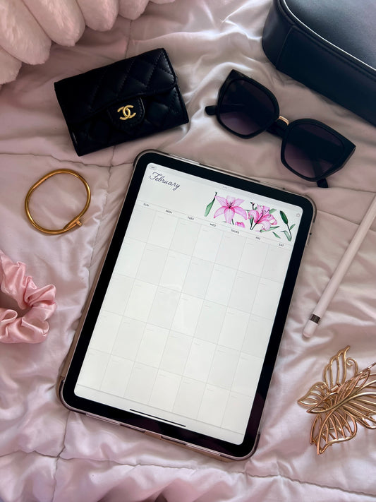 Tablet displaying February month of calendar on a bed with various accessories around.