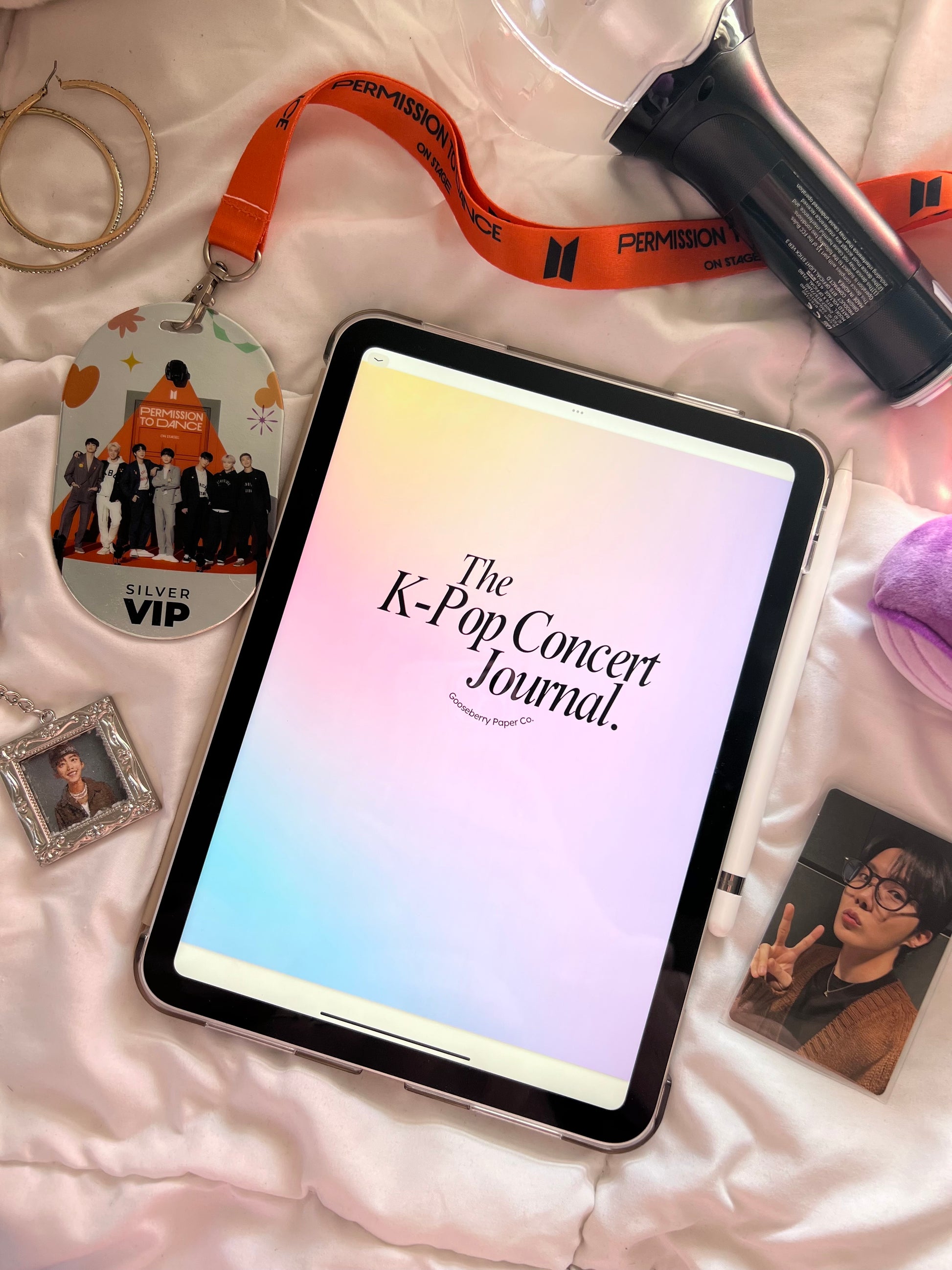 Tablet displaying K-Pop Concert Journal on a bed with various K-Pop merch items around.