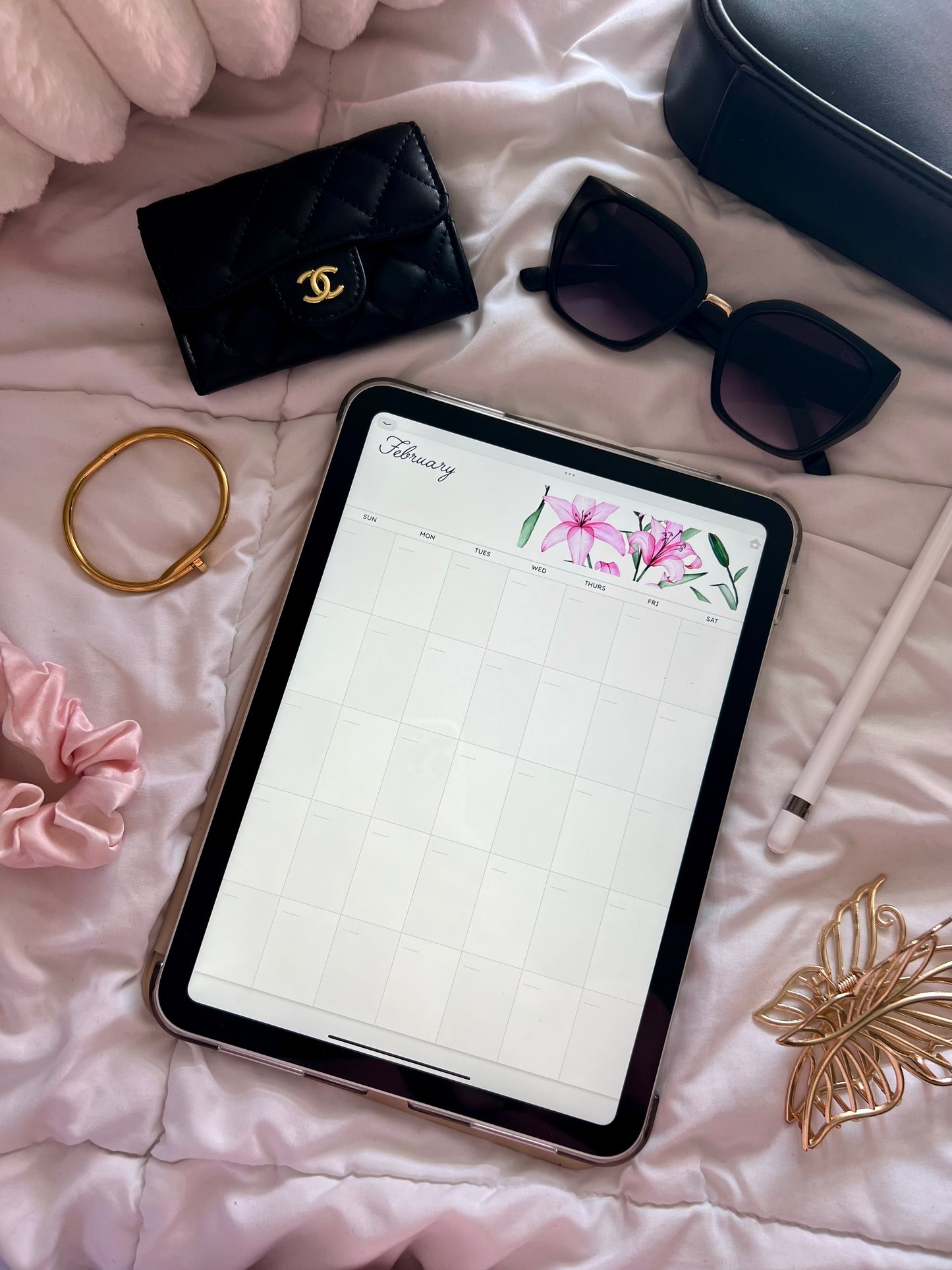 Tablet displaying February month of calendar on a bed with various accessories around.