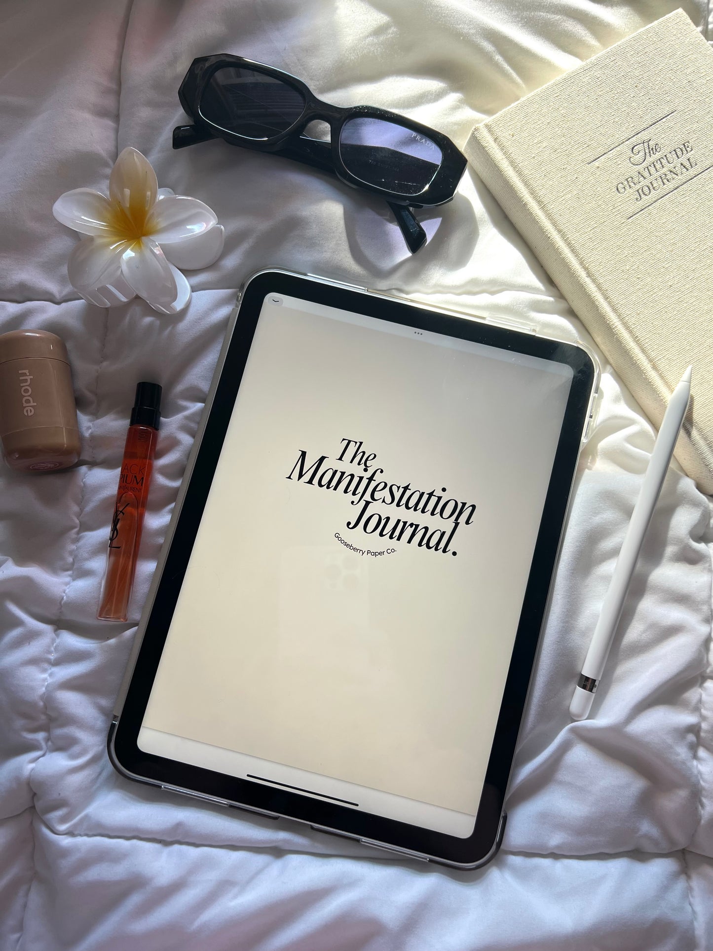 Tablet displaying Manifestation Journal on a bed with various items around.