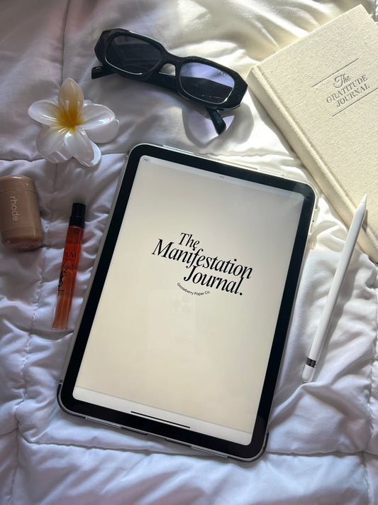 Tablet displaying Manifestation Journal on a bed with various items around.