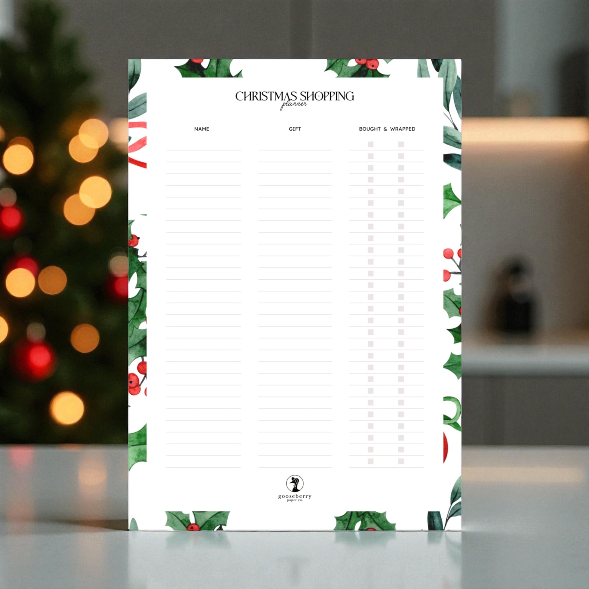Mockup of blank printable Christmas shopping list with festive border on a blurred background.