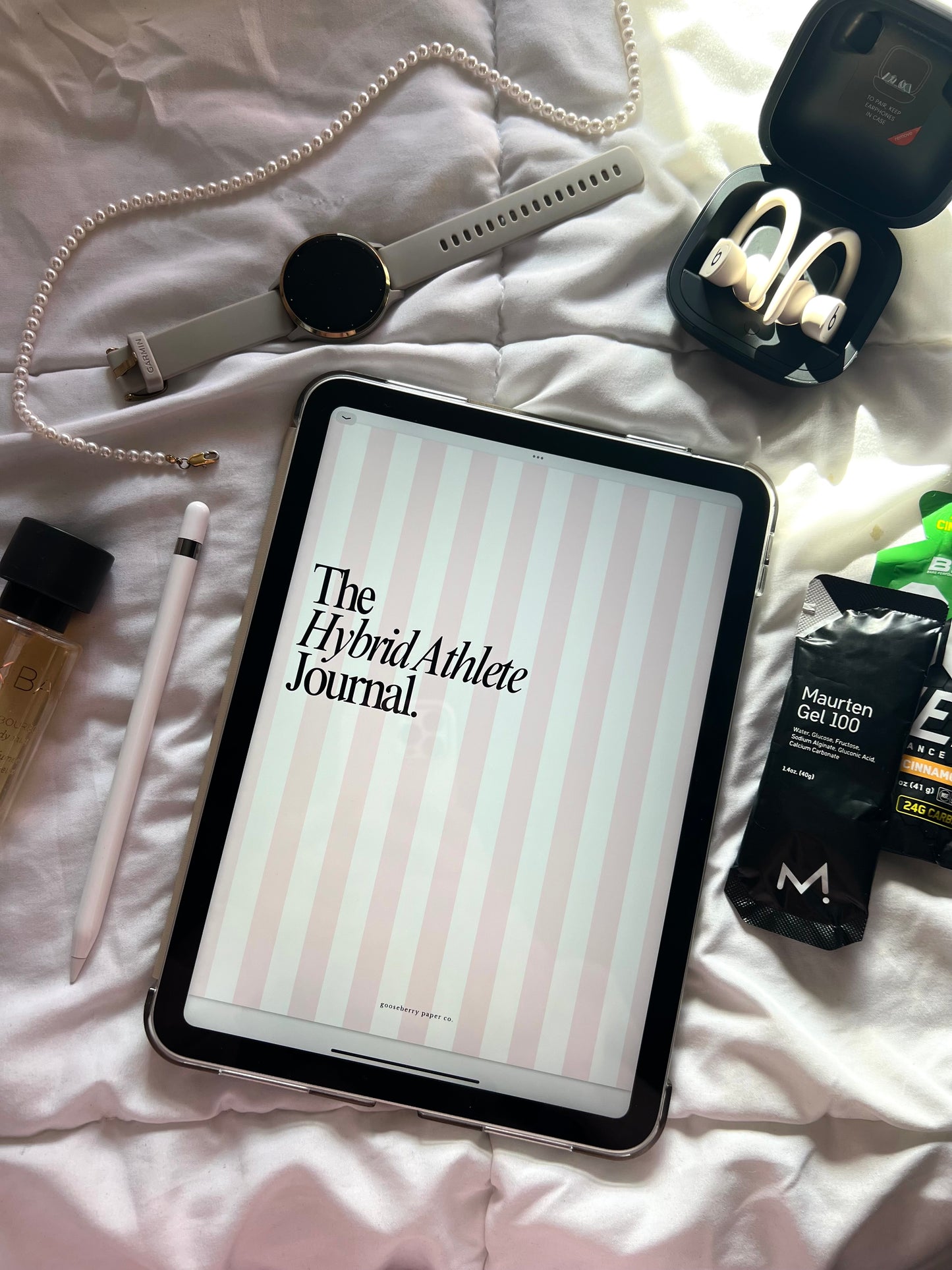 Tablet displaying The Hybrid Athlete Journal on a bed with various fitness items around.